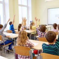group-of-school-kids-raising-hands-in-classroom-PF36XQ9